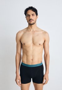 Black underwear with a turquoise waistband featuring "BJÖRN BORG" text. Soft fabric, fitted design, and mid-thigh length.