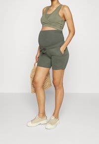Olivově zelený těhotenský top s překříženým designem, spárovaný s odpovídajícími šortkami s elastickým pasem a kapsami.