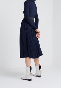 Marinblå långärmad klänning med en utsvängd kjol, kombinerad med vita ankelskor med svarta accenter och snörebandsfästen bak.