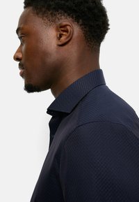 Marineblaues Hemd mit einem strukturierten, Rautenmuster; verfügt über einen spitzen Kragen und eine sichtbare Knopfleiste; elegantes, tailliertes Design.