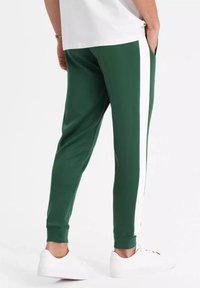 Gröna joggerbyxor med vita sidostrimmor, tillverkade av mjukt material. Har avsmalnande ben och ribbade mudd; portas med vita sneakers.