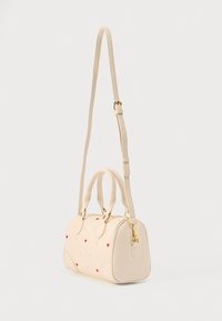 Τσάντα χειρός σε κρεμ χρώμα με στρογγυλεμένο σχήμα, διακοσμημένη με μικρά κόκκινα μοτίβα καρδιάς. Διαθέτει δύο λαβές στην κορυφή και αποσπώμενο ιμάντα με χρυσές μεταλλικές λεπτομέρειες.