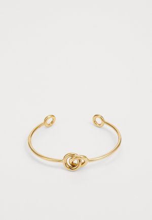 Złoty bransoletka na nadgarstek wykonana z metalu, z centralnym wzorem w kształcie węzła i otwartymi końcami z okrągłymi akcentami. Gładka, błyszcząca tekstura.