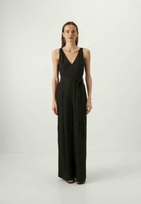 Svart ermeløs jumpsuit med V-hals og knytedetalj i livet. Laget av glatt stoff; vid benlengde og flytende design. Ingen synlige mønstre eller maskinvare.