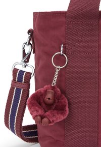 Borsa in tessuto bordeaux con una tracolla intrecciata caratterizzata da strisce blu marino e crema, impreziosita da un portachiavi a forma di gorilla in peluche attaccato a un anello in argento.