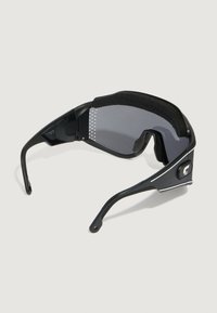 Occhiali da sole neri con un design elegante, dotati di ponte nasale imbottito, lenti grigie e accenti laterali prominenti. Telaio leggero.