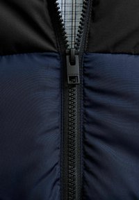 Granatowa i czarna kurtka puchowa z centralnym zamkiem błyskawicznym, teksturowaną tkaniną i kratkowaną, wewnętrzną podszewką. Wyróżniające się okucia z nazwą marki.