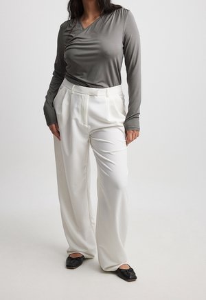 Maglione grigio a maniche lunghe con scollatura a V, abbinato a pantaloni bianchi a vita alta e a gamba larga. Scarpe flat nere con fiocchi completano l'outfit.