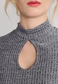 Szary top w wzór z wysokim kołnierzem i wycięciem w kształcie klucza przy dekolcie. Materiał wydaje się fakturowany z pionowymi paskami.