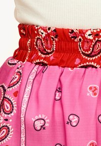 Falda rosa con cintura elástica roja. Presenta patrones de paisley y pequeños elementos decorativos en colores contrastantes. Textura suave.