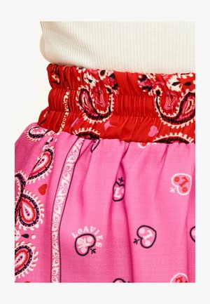 Jupe rose avec une taille élastique rouge. Elle présente des motifs paisley et de petits éléments décoratifs dans des couleurs contrastées. Texture lisse.