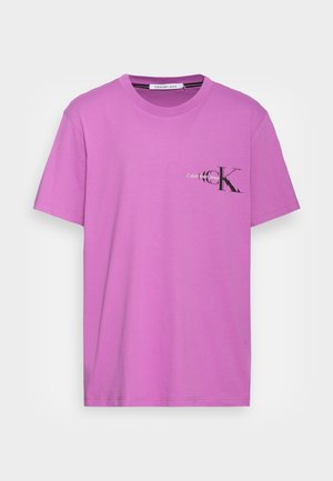 Fioletowa bawełniana koszulka z krótkim rękawem, z czarnym logo "CK" oraz napisem "Calvin Klein Jeans" po lewej stronie klatki piersiowej.