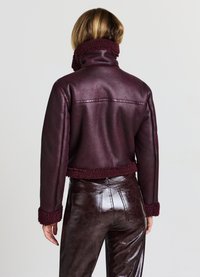 Veste en simili cuir bordeaux avec un col et des poignets peluchés, design court et texture lisse. Associée à un pantalon en cuir brun brillant.