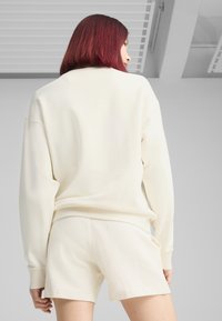 Světle krémová mikina a odpovídající šortky, obojí vyrobené z měkkého materiálu s volným střihem. Design zahrnuje spadlé ramena a jednoduchou siluetu.