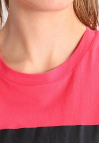 Kortärmad T-shirt med en bred, rund halsringning, tillverkad av bomull i klar rosa med en svart panel nedtill. Slät textur.