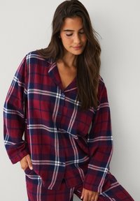 Rode en marineblauwe geruite flanellen pyjama-top met lange mouwen, een kraag en knoopsluitingen. Zachte textuur en een losse pasvorm.