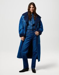 Denim buitenkleding set met een oversized blauwe jas met een zwarte schapenvacht kraag, gecombineerd met een bijpassende blauwe shirt en jeans.