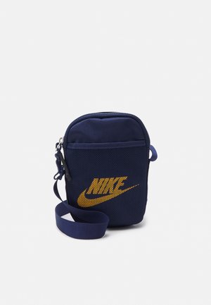 Petit sac bandoulière bleu marine avec logo Nike orange, poche avant zippée et sangle réglable sur fond blanc.