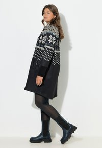 Knælang sort kjole med en strikket mønstret overdel i grå og blå, med lange ærmer og sidelommer, kombineret med blå ankelstøvler.