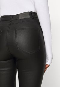 Leggings de imitación cuero negro que presentan un diseño ajustado, dos bolsillos traseros y una textura suave. Una pequeña etiqueta de la marca es visible en la cintura.