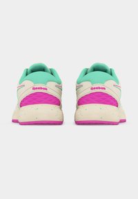 Ζευγάρι κρεμ αθλητικών παπουτσιών Reebok με ροζ σόλες, ροζ και πράσινες λεπτομέρειες, και πράσινους επενδυμένους γιακάδες, εμφανιζόμενα από πίσω σε λευκό φόντο.