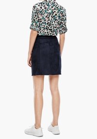 Minifalda de ante azul marino con detalles de costura sutiles, combinada con una blusa a rayas en blanco y negro. Zapatillas blancas completan el conjunto.