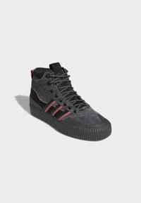 Zapatillas altas de ante gris oscuro con acentos en negro, suela de goma texturizada, cordones en blanco y negro, y tres franjas rojas en el lateral.