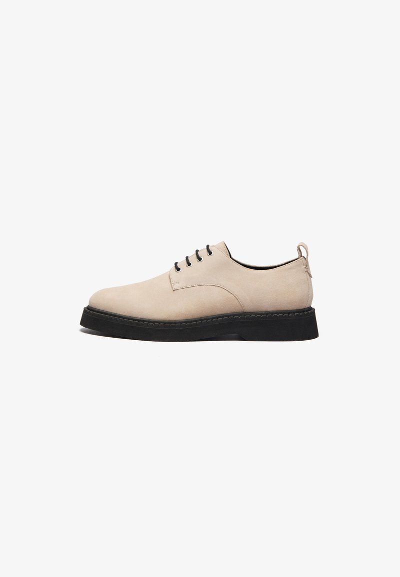 Scarpa in suede beige con lacci, punta rotonda, suola in gomma nera e sei fori per i lacci, dotata di una linguetta sul retro per facilitarne l'indossamento.