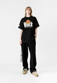 Camiseta negra de gran tamaño con un gráfico colorido de un perro y texto en blanco. Combinada con pantalones negros holgados y zapatillas multicolores.