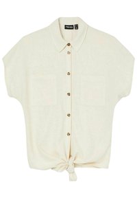 Short-sleeve beige shirt with a button-up front, two chest pockets, and a knotted hem detail. Made from lightweight, textured fabric.