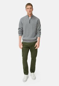 Grijze geribde pullover trui met een halve rits nek, gecombineerd met olijfgroene cargobroeken met zijzakken, en witte sneakers.