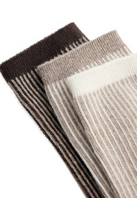 Trei șosete tricotate cu nervuri, pliate, în culorile maro închis, bej și alb-crem, aranjate suprapuse pe un fundal alb.