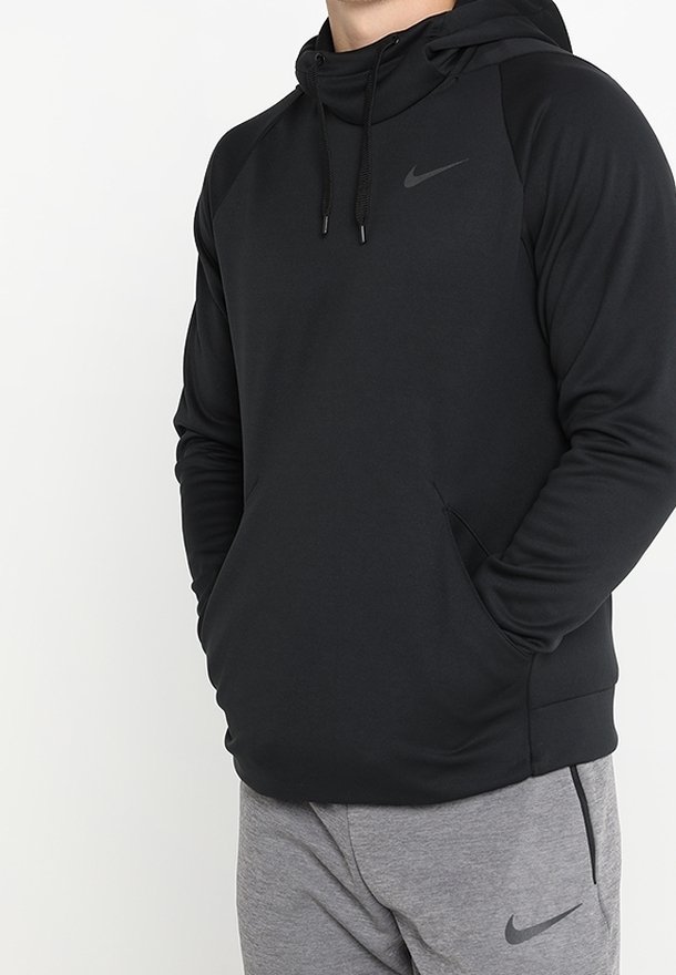 Homme portant un sweat à capuche Nike noir avec cordons et un pantalon de survêtement Nike gris, les mains dans la poche du sweat.