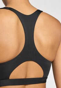 Top deportivo negro con diseño racerback y detalles de cortes. Hecho de tela texturizada con un acabado suave. Banda ajustable.