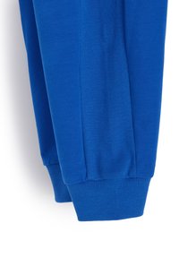 Niebieskie sportowe spodnie z gładką i prążkowaną fakturą, zawierające prążkowane mankiety przy kostkach oraz boczny panel w designie.