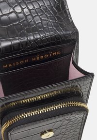 Black crocodile-printed leather bag with a zippered compartment, gold hardware, and a soft pink interior. Features a brand label inside.