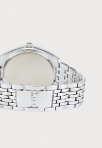 Montre en métal argenté avec un boîtier rectangulaire, bracelet en maillons entrelacés et finition polie. Design minimaliste sans marquages visibles.