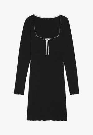 Svart ribbestrikket langermet kjole med firkantet utringning, hvit snor detalj, og bølget mansjetter ved ermene og nederkant.