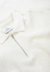 Hellbeige Zip-Up-Polo aus strukturiertem Strickstoff. Verfügt über einen schlichten Kragen und einen silbernen Reißverschluss. Markenlabel innen am Kragen sichtbar.