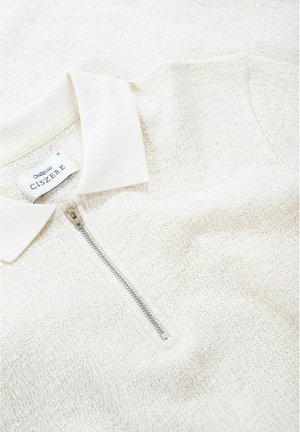 Jasno beżowa polo na zamek błyskawiczny z teksturowanej dzianiny. Posiada gładki kołnierzyk oraz srebrny zamek. Etykieta marki widoczna wewnątrz kołnierza.