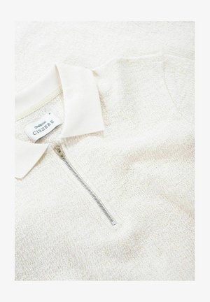 Jasno beżowa polo na zamek błyskawiczny z teksturowanej dzianiny. Posiada gładki kołnierzyk oraz srebrny zamek. Etykieta marki widoczna wewnątrz kołnierza.