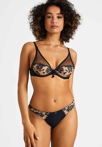 Ensemble de lingerie noire avec tissu transparent, broderie florale et garniture décorative. Le soutien-gorge présente un design décolleté avec des bretelles ajustables.