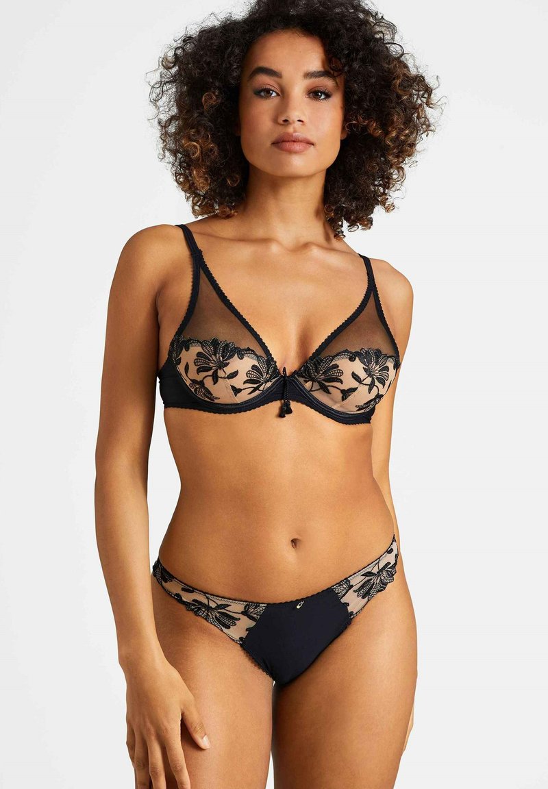 Ensemble de lingerie noire avec tissu transparent, broderie florale et garniture décorative. Le soutien-gorge présente un design décolleté avec des bretelles ajustables.