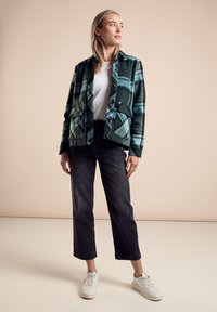 Groene en blauwe geruite jas met voorzakken, gecombineerd met zwarte cropped broeken en witte sneakers. Gladde stof, knoopsluitingen, casual ontwerp.