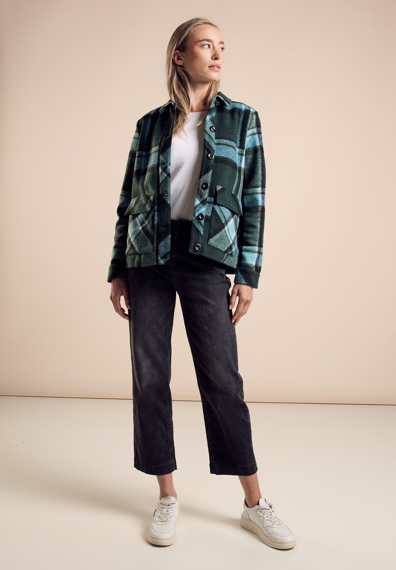 Groene en blauwe geruite jas met voorzakken, gecombineerd met zwarte cropped broeken en witte sneakers. Gladde stof, knoopsluitingen, casual ontwerp.