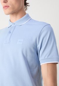 Polo shirt azzurro chiaro realizzato in tessuto testurizzato. Dotato di un colletto classico con bordatura bianca, due bottoni e un piccolo logo del marchio sul petto.
