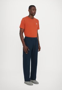 Oranges Crew-Neck T-Shirt, navyfarbene Hose mit elastischem Bund, graue Sneaker. Weicher, lässiger Schnitt mit einfachem Design und ohne sichtbare Muster.