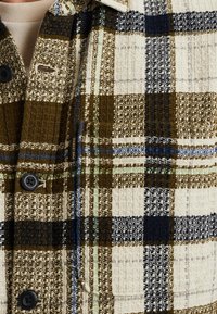 Geruite shirt met een bruin, marineblauwe en crème kleurenschema, gemaakt van textuurstof, met knoopsluiting en subtiele logo-details op de zak.
