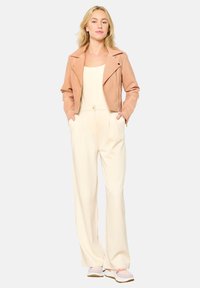 Chaqueta de cuero sintético rosa claro, top crema ajustado, pantalones crema de cintura alta y zapatillas blancas con acentos en tonos pastel.