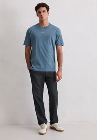 Niebieski bawełniany T-shirt z krótkimi rękawami i okrągłym dekoltem, w połączeniu z ciemnoszarymi spodniami i białymi trampkami. Proste logo na koszulce.